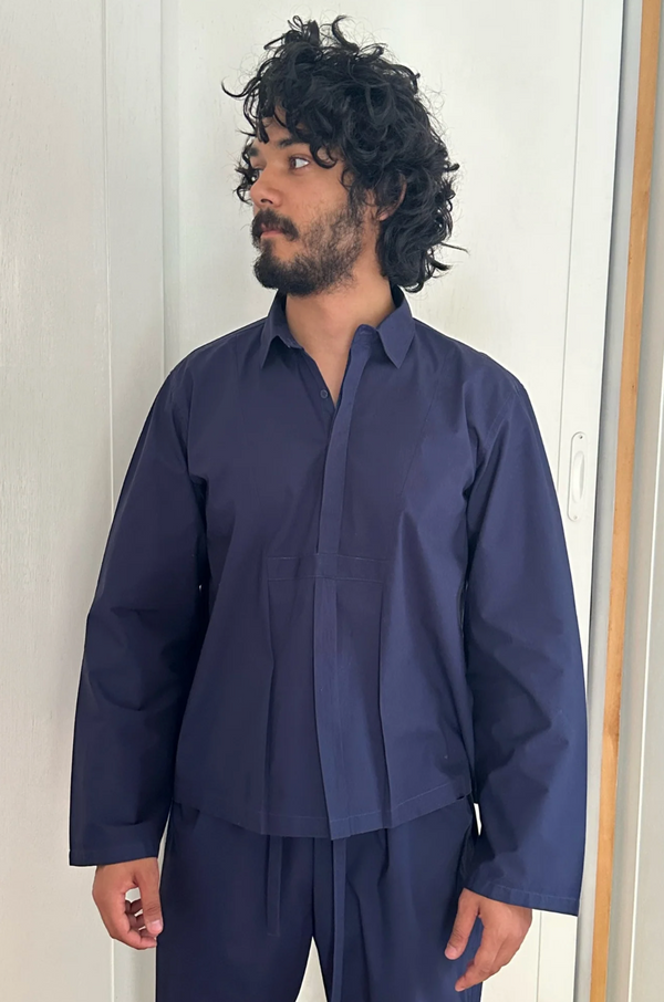 Man wearing a navy blue shirt and pants against a white wall.