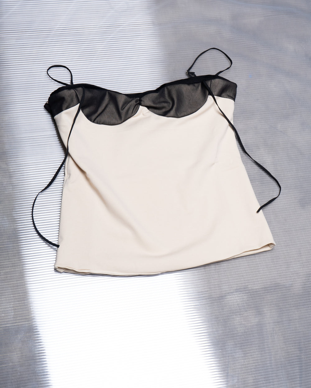 A beige body-fitted double fabric nude top with black mesh and black elastic straps, displayed on a flat surface.