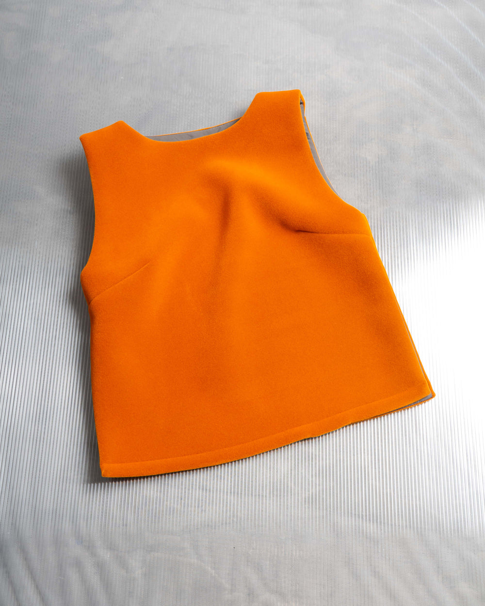 An orange, sleeveless neoprene side split top displayed on a flat surface.